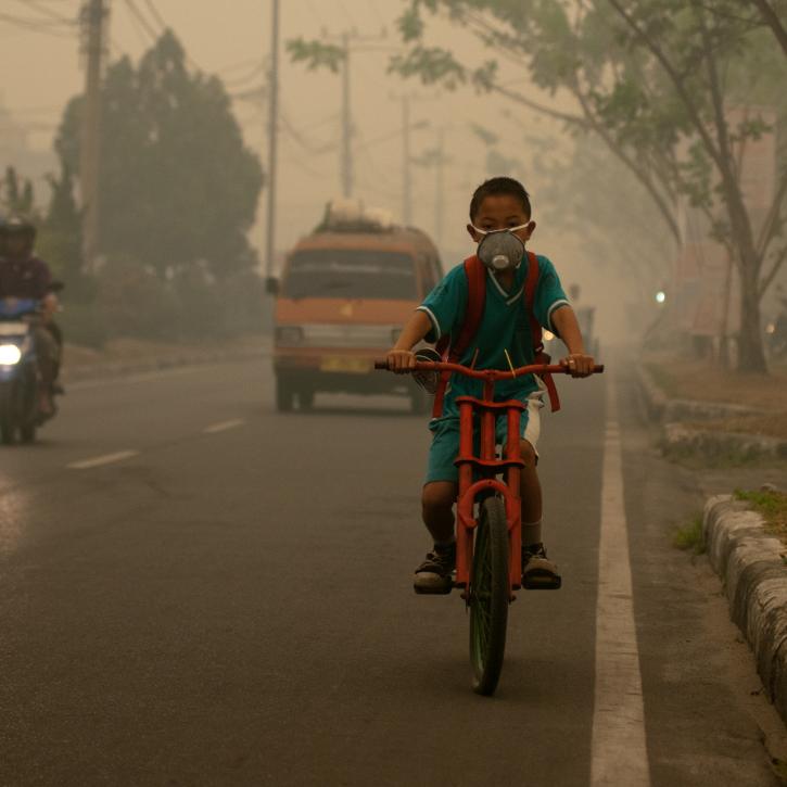 Boy cycling through smoke with a mask