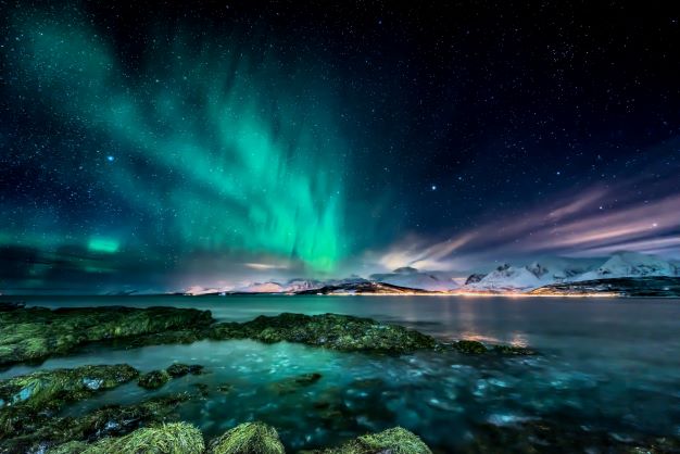Northern lights above snowy mountains and blue water