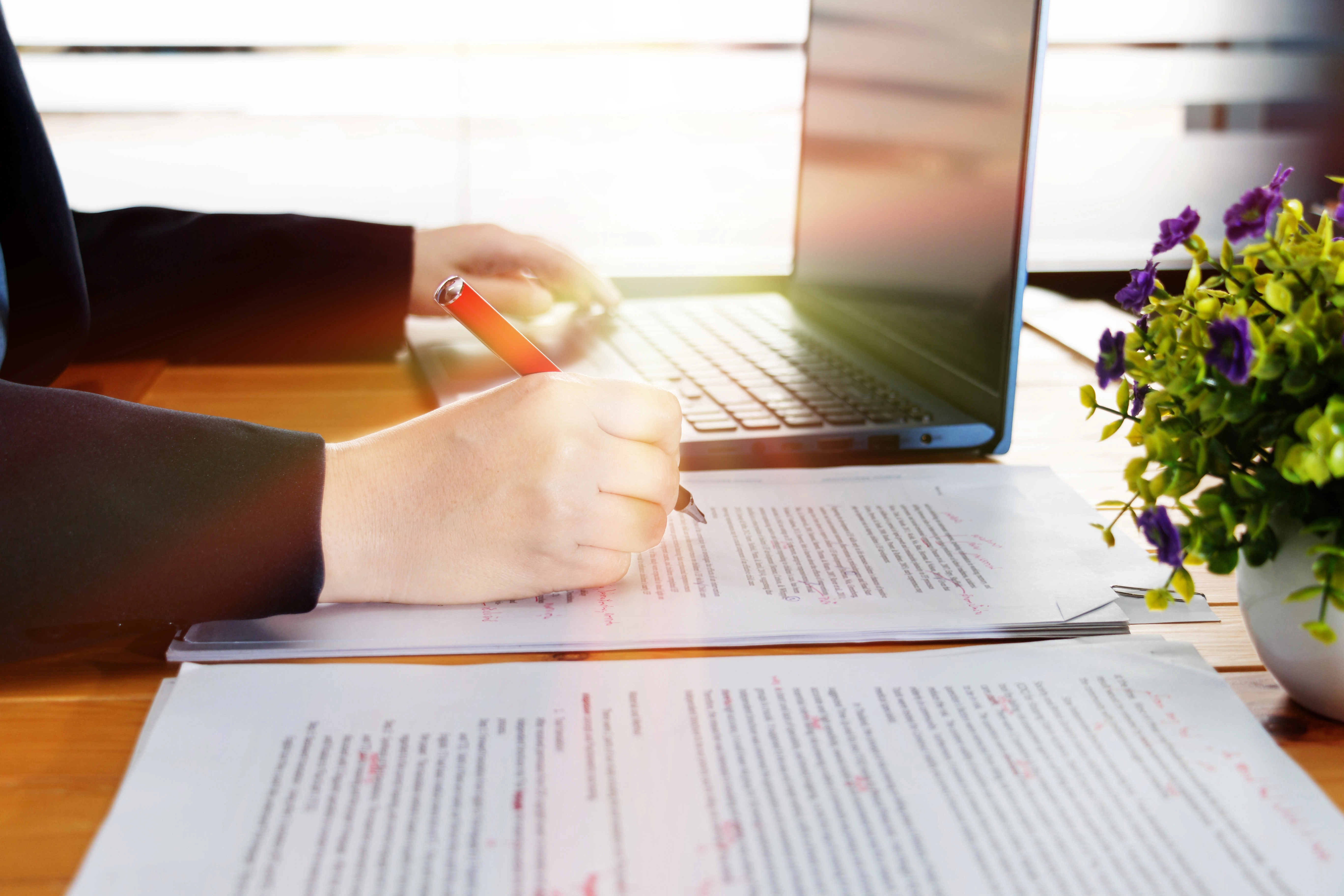 Hand editing document on desk with laptop in background