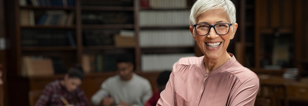 A lady smiles in front of library bookshelves and students