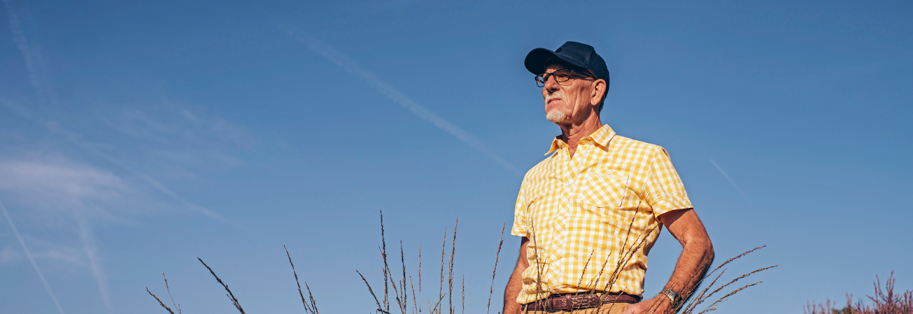 An elderly man in a baseball hat looks out over the fields