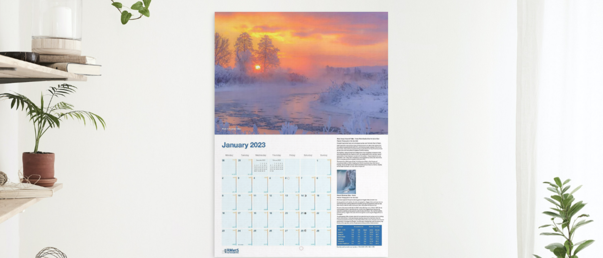 January's page showing a colourful frosty river scene with the calendar grid below. It is shown hanging on a wall