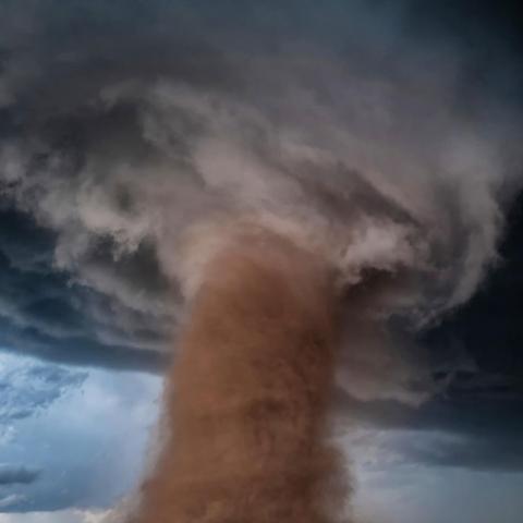 A large, dust-filled tornado turns across an open field in Wray, Colorado