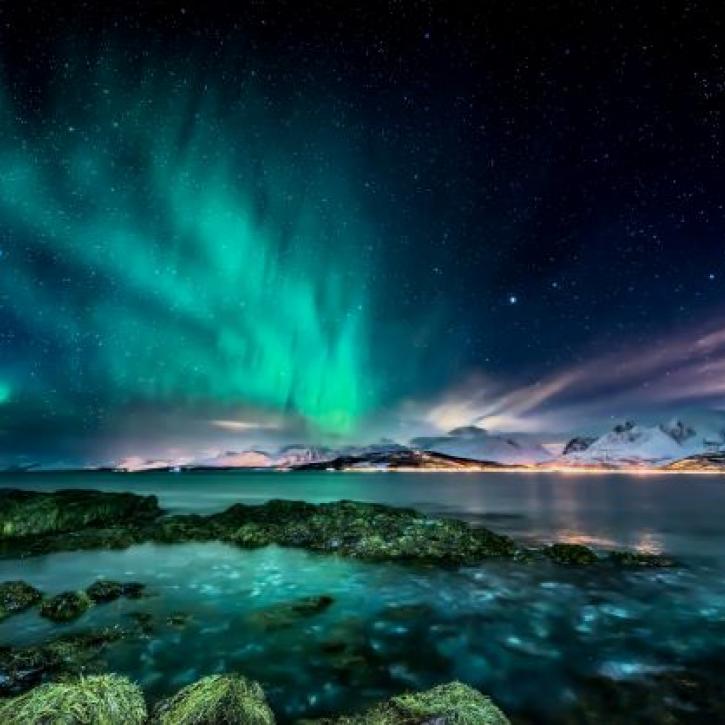 Northern Lights above snowy mountains and blue water